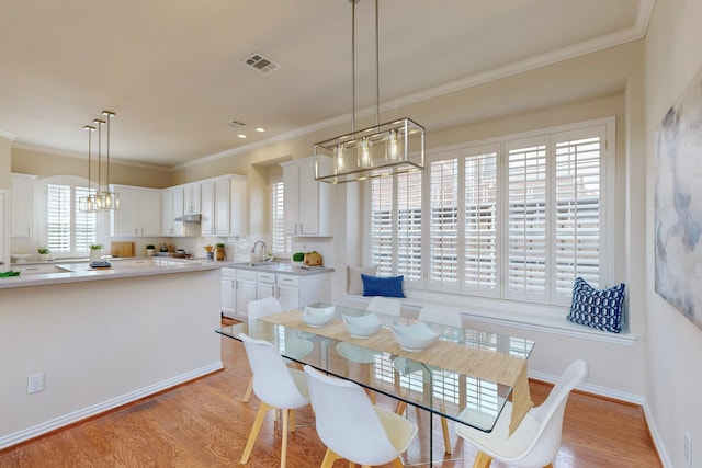 dining space with light wood-type flooring, visible vents, a notable chandelier, crown molding, and baseboards