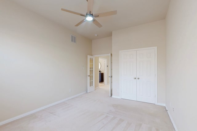 unfurnished bedroom featuring visible vents, light carpet, a closet, baseboards, and ceiling fan