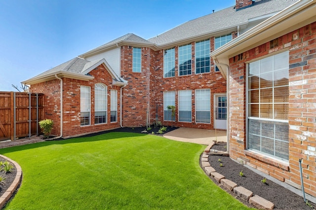 back of house with a lawn, a patio, fence, roof with shingles, and brick siding