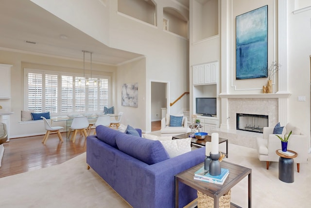 living area with wood finished floors, a fireplace, a towering ceiling, and ornamental molding