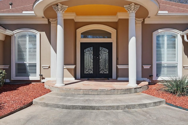 view of exterior entry featuring stucco siding, roof with shingles, and a porch