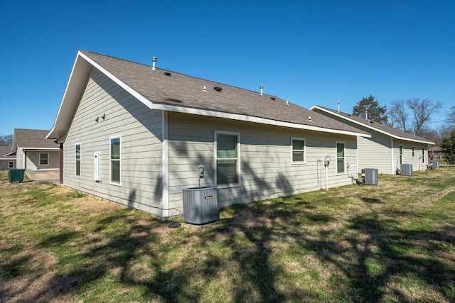 back of property featuring a yard, central AC unit, and a shingled roof