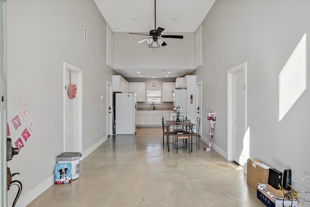 dining area featuring visible vents, finished concrete flooring, ceiling fan, baseboards, and a high ceiling