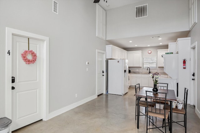 dining area with visible vents, concrete flooring, a high ceiling, and baseboards