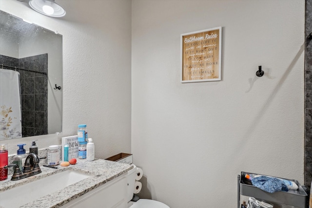 bathroom with vanity, toilet, a textured wall, and tiled shower