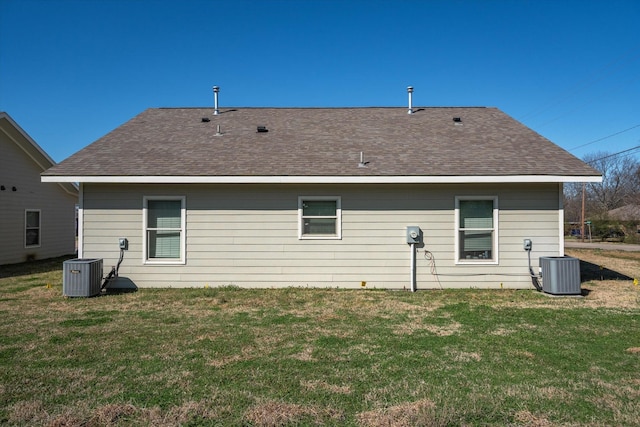 rear view of house featuring central AC unit, a lawn, and roof with shingles