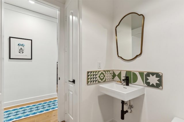 bathroom featuring tasteful backsplash, a sink, baseboards, and wood finished floors