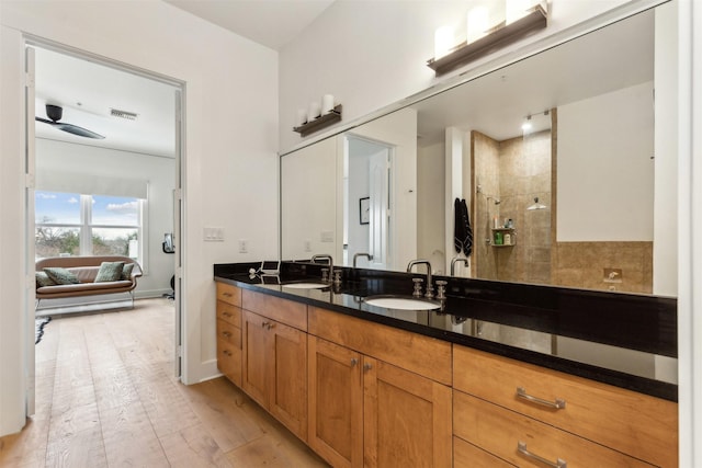 bathroom featuring wood finished floors, visible vents, double vanity, a sink, and a walk in shower