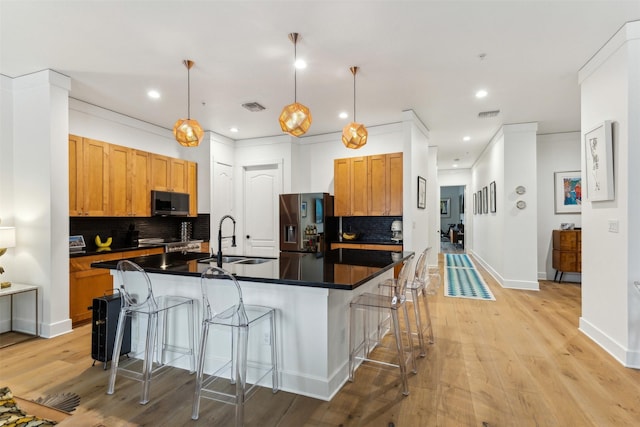 kitchen with a breakfast bar, a kitchen island with sink, a sink, stainless steel appliances, and dark countertops