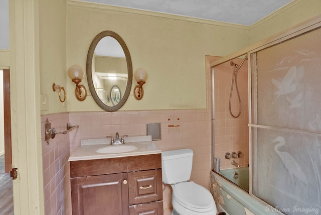 full bathroom featuring a wainscoted wall, shower / bath combination with glass door, tile walls, and vanity