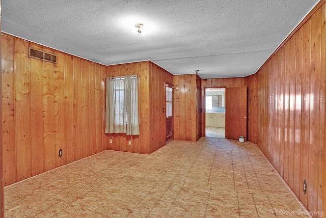 empty room featuring tile patterned floors, visible vents, and wooden walls