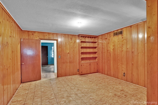 spare room with tile patterned floors, visible vents, wooden walls, and a textured ceiling