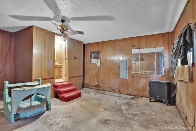 interior space featuring wooden walls, concrete floors, electric panel, ceiling fan, and a textured ceiling