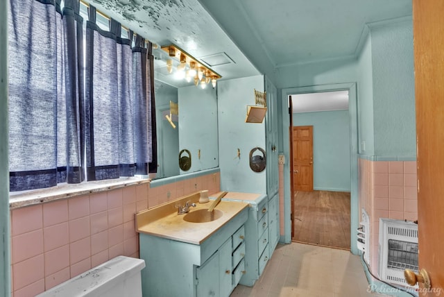 bathroom with heating unit, toilet, tile walls, and vanity