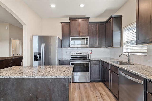 kitchen featuring light wood finished floors, dark brown cabinets, light stone countertops, appliances with stainless steel finishes, and a sink