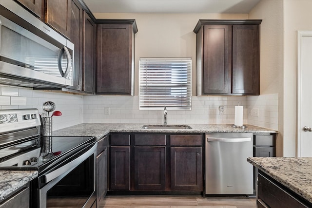 kitchen with a sink, tasteful backsplash, appliances with stainless steel finishes, light stone countertops, and dark brown cabinets