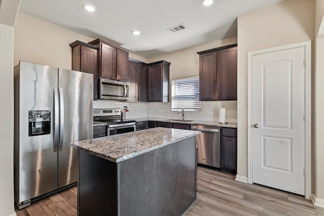 kitchen featuring backsplash, light stone countertops, dark brown cabinetry, appliances with stainless steel finishes, and a sink