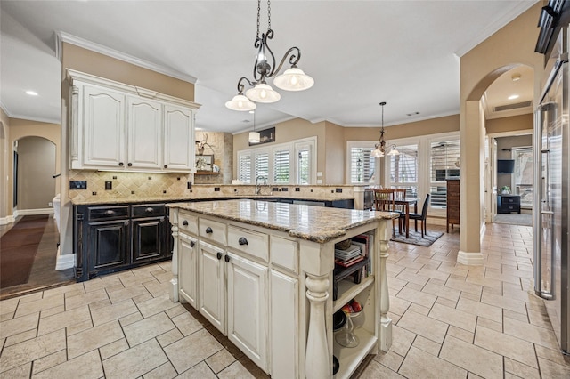 kitchen featuring tasteful backsplash, open shelves, light stone countertops, arched walkways, and a sink