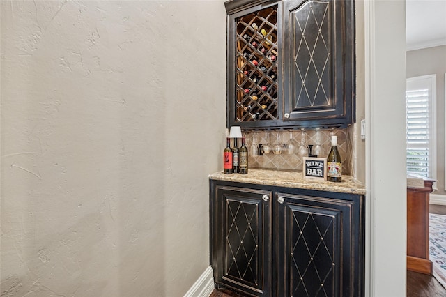 bar with tasteful backsplash, wood finished floors, a bar, crown molding, and baseboards