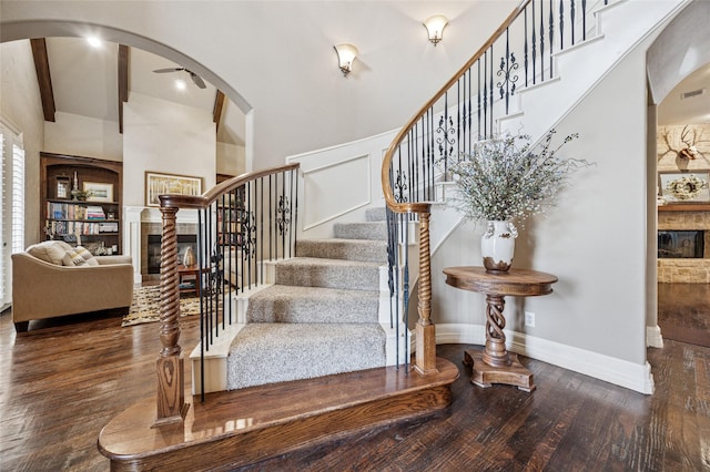 stairs with baseboards, hardwood / wood-style floors, beam ceiling, a towering ceiling, and arched walkways