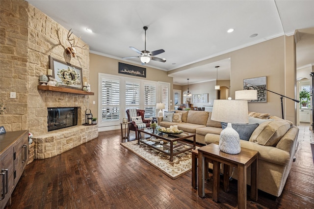 living room featuring a ceiling fan, dark wood finished floors, recessed lighting, a stone fireplace, and crown molding