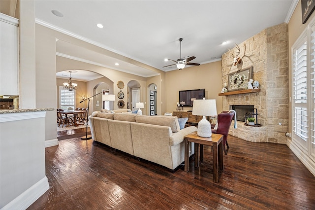 living room featuring baseboards, ornamental molding, a stone fireplace, arched walkways, and dark wood-style flooring