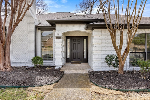 doorway to property with brick siding and a shingled roof