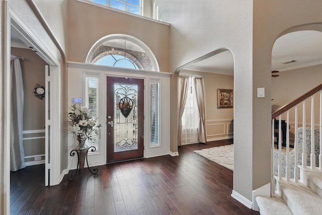 foyer featuring stairway, a healthy amount of sunlight, dark wood-style flooring, and crown molding