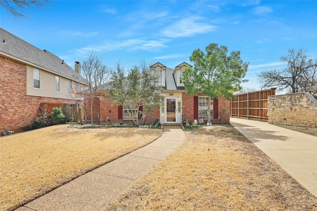 view of front facade featuring fence, brick siding, and a shingled roof