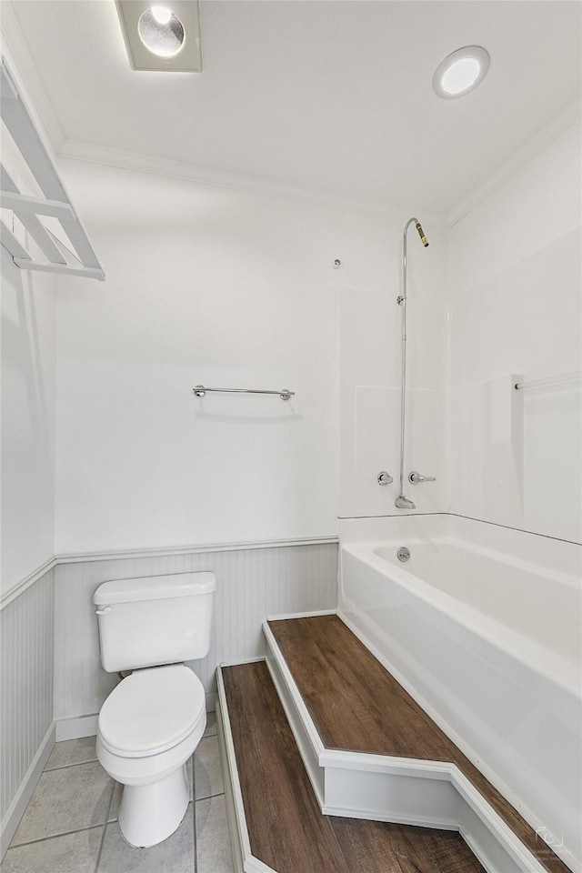 bathroom with tile patterned floors, toilet, tub / shower combination, and a wainscoted wall