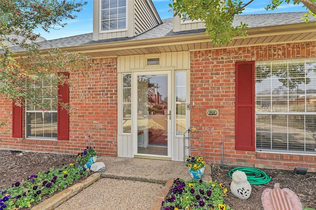 property entrance featuring board and batten siding, brick siding, and a shingled roof