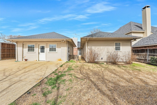 back of property with a patio area, roof with shingles, a yard, and fence