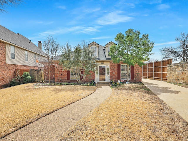 view of front of home featuring brick siding, a shingled roof, and fence