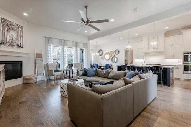 living area with a glass covered fireplace, ceiling fan with notable chandelier, crown molding, and wood finished floors