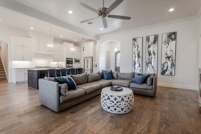 living area with arched walkways, crown molding, and dark wood-style flooring