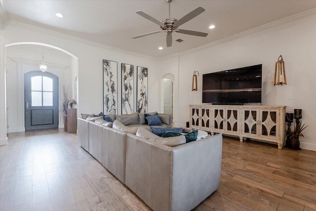 living area featuring arched walkways, light wood-style floors, and crown molding