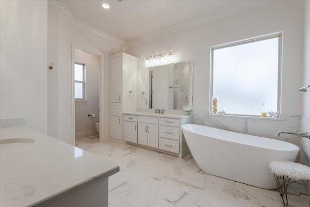 full bath with a freestanding bath, two vanities, ornamental molding, marble finish floor, and a sink