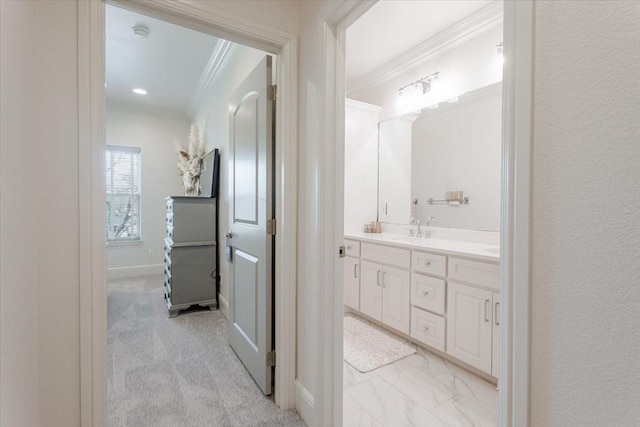 bathroom featuring marble finish floor, a sink, crown molding, double vanity, and baseboards