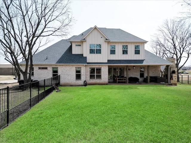 rear view of property featuring brick siding, a lawn, board and batten siding, and a fenced backyard