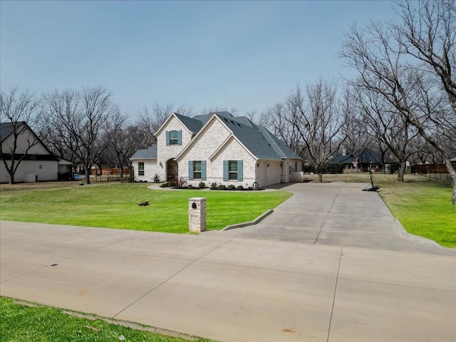 french provincial home featuring a garage, stone siding, concrete driveway, and a front lawn