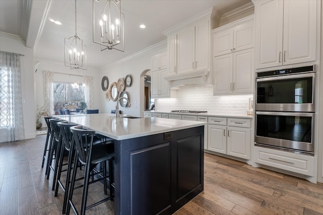 kitchen with an island with sink, a sink, tasteful backsplash, stainless steel appliances, and arched walkways