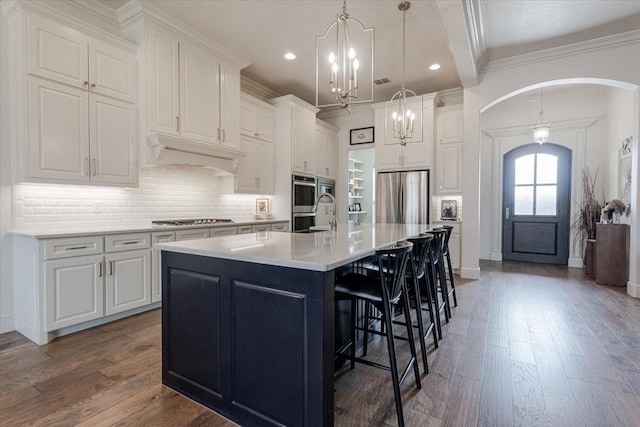 kitchen with under cabinet range hood, wood finished floors, stainless steel appliances, arched walkways, and white cabinets