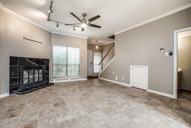 unfurnished living room with stairway, a ceiling fan, baseboards, a tiled fireplace, and crown molding