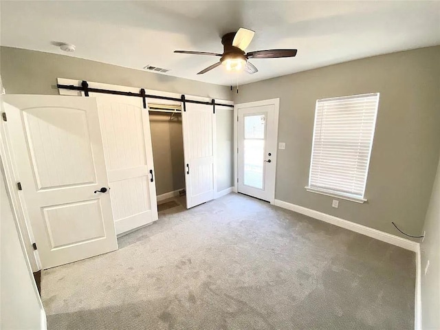 unfurnished bedroom featuring visible vents, ceiling fan, baseboards, a barn door, and carpet floors