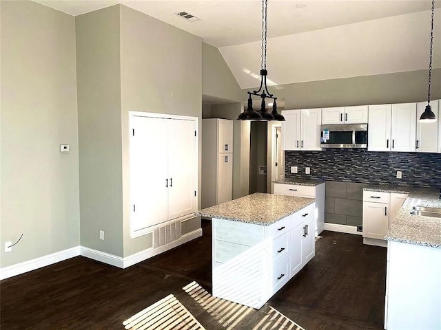 kitchen featuring stainless steel microwave, light stone counters, dark wood-style flooring, and vaulted ceiling