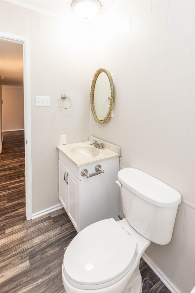 half bath featuring toilet, vanity, baseboards, and wood finished floors