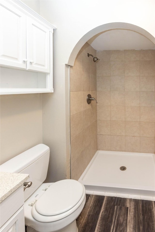 full bathroom with tiled shower, toilet, vanity, and wood finished floors