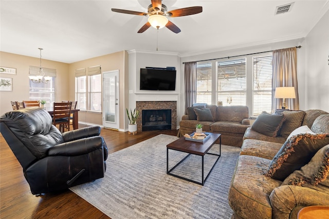 living area with wood finished floors, visible vents, a fireplace, crown molding, and ceiling fan with notable chandelier