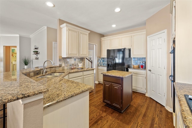 kitchen featuring light stone counters, a peninsula, a sink, dark wood-type flooring, and black fridge with ice dispenser