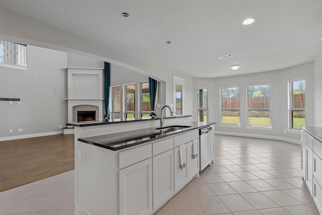 kitchen with a sink, open floor plan, light tile patterned floors, a fireplace, and stainless steel dishwasher